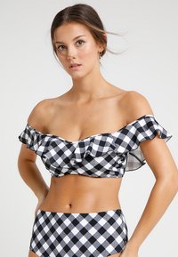 Conjunto de biquíni preto e branco com padrão xadrez, apresentando um top off-shoulder com babados e parte de baixo de cintura alta combinando. Tecido suave com acabamento mate.