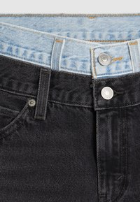 Svarta denimjeans med en ljusblå midja, med silverdetaljer, kontrastsömmar och en slät textur nära toppen.