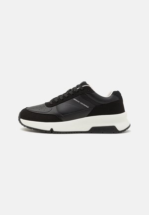 Zapatilla Armani Exchange en negro y gris oscuro con suela blanca gruesa y cierre de cordones, nombre de la marca visible en el lateral y en la suela.