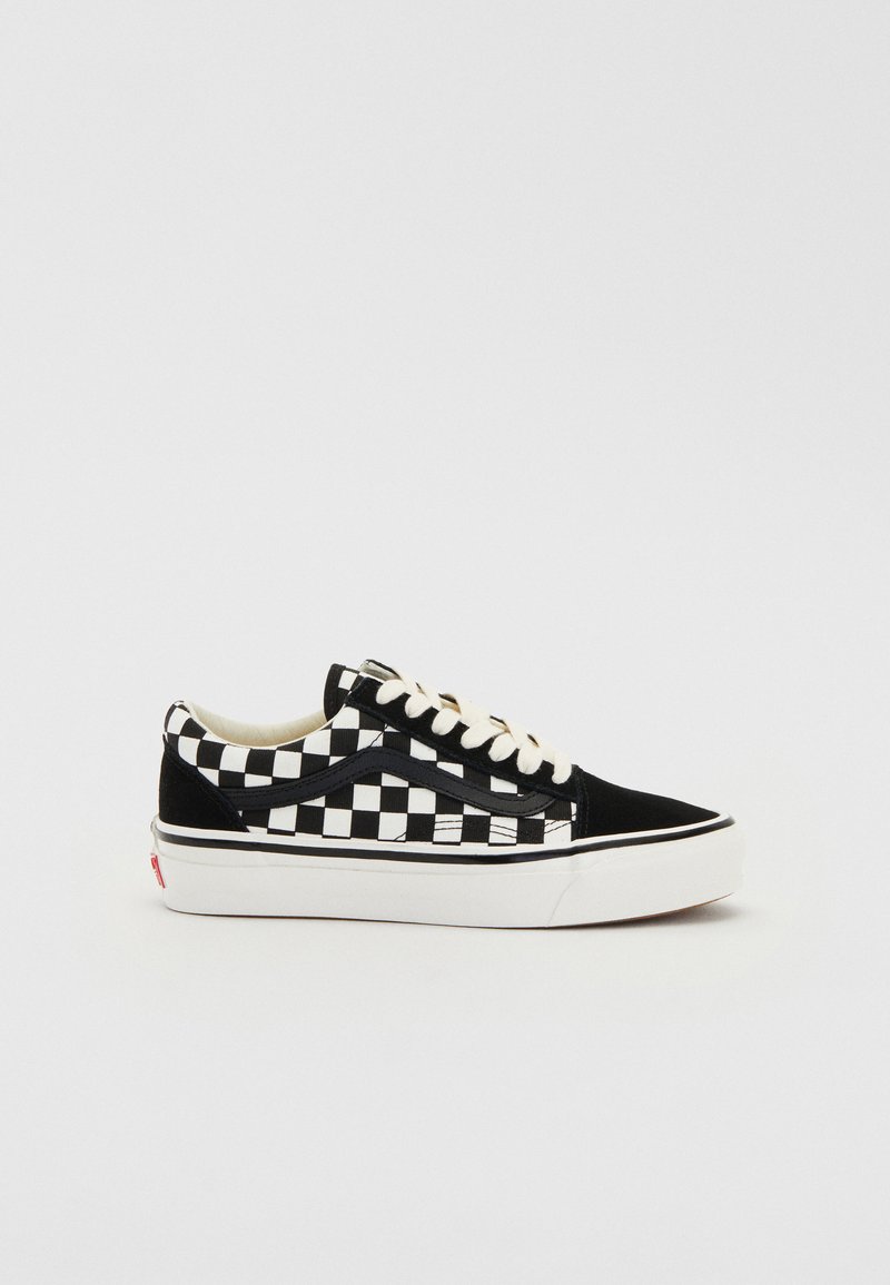Zapatillas de cuadros en blanco y negro con parte superior de lona, suela de goma y cordones blancos. Raya lateral acentuada en negro. Diseño clásico de caña baja.