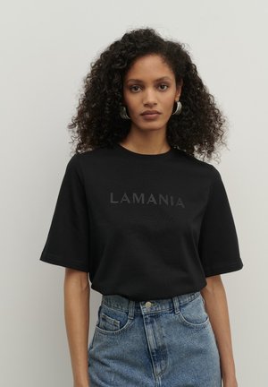 Czarny t-shirt z krótkim rękawem z napisem "LAMANIA" na przodzie, w połączeniu z niebieskimi dżinsowymi szortami o wysokim stanie. Gładka tekstura, luźny krój.