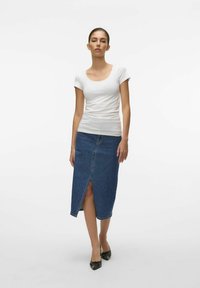 T-shirt bianco con scollo a barchetta abbinato a una gonna in denim blu con uno spacco frontale e orlo dritto, indossato con scarpe nere a punta.