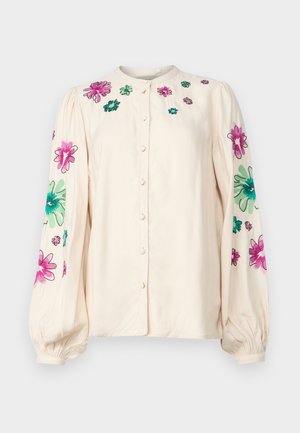 Kremowa koszula z okrągłym dekoltem, długimi bufkami i intensywnym haftem kwiatowym w różowym i zielonym kolorze na ramionach i rękawach.
