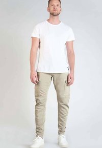 Lichtgewicht wit katoenen T-shirt gecombineerd met nauwsluitende beige cargobroek met zijzakken en taps toelopende pijpen. Draagt witte sneakers.