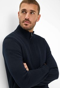 Marine blauwe zip-up trui met hoge kraag, ribbeltextuur bij de kraag en manchetten, en een gladde stof voor het lichaam. Getailleerd ontwerp met lange mouwen.