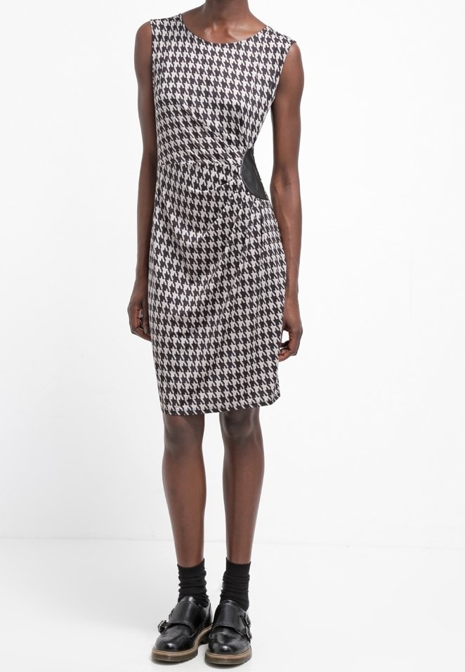Šaty s černobílým vzorem houndstooth, fitted siluetou a bočním výřezem, doplněné černými ponožkami a mokasínami.