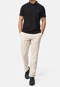 Svart polo med röda accenter, smal passform, två-knapps hals, i kombination med ljus beige byxor och svarta sneakers. Platt textur, klassisk design.
