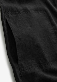 Gros plan sur un tissu en lin noir montrant une fente latérale et des coutures détaillées.