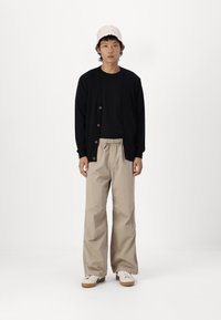 Svart cardigan over en svart t-skjorte, beige vidbukser og kremfargede sko. Bruker en teksturert lys rosa bøttehatt.