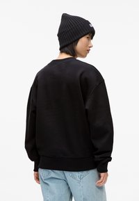 Melnā sporta krekls ar ribotu apkakli un nolaistām plecu šuvēm. Apvienots ar gaiši ziliem džinsiem, modelis valkā melnu ribotu cepuri.