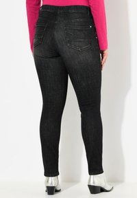 Jeans skinny de denim negro con una cintura alta, que cuentan con dos bolsillos traseros y una textura sutil. Combinados con botines de tacón plateados.