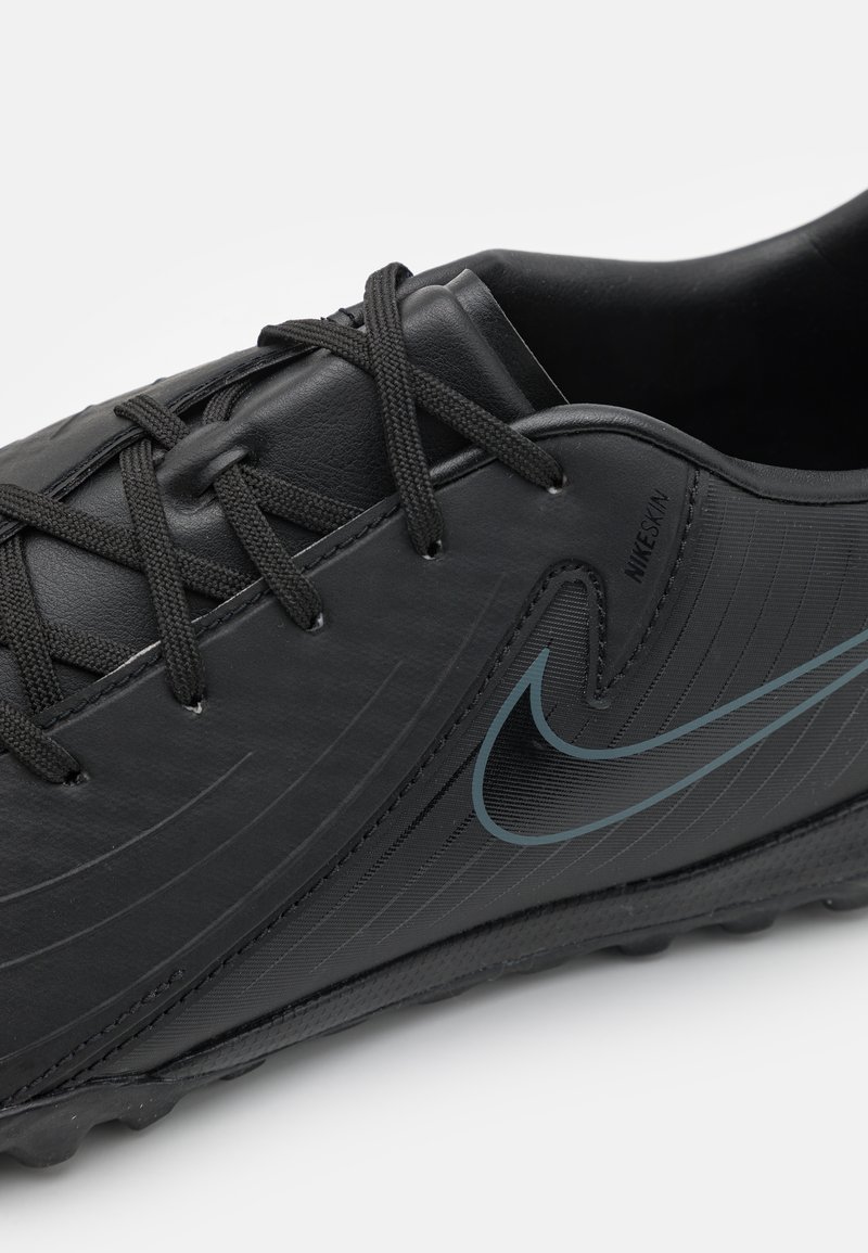 Botín de fútbol negro con parte superior de cuero texturizado, cordones negros, un discreto swoosh azul de Nike y una suela de goma con pequeñas puntas.