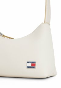 Biała torba na ramię z imitacji skóry o zaokrąglonym kształcie, z metalowym logo Tommy Jeans. Gładka faktura, minimalistyczny design.