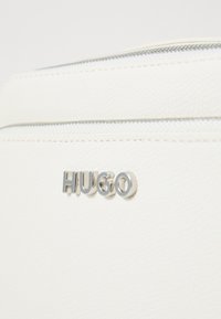 Witte gestructureerde leren tas met een zilveren ritssluiting en een zilveren "HUGO" logo. Het oppervlak heeft een gemarmerde afwerking.