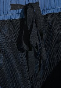 Blå midjeband med svart nätmaterial nedanför. Har en svart dragsko med plastspetsar, vilket framhäver den andningsbara texturen och det lager-på-lager design.