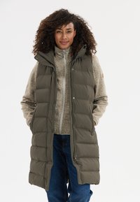 Ärmellose Steppjacke in Olivgrün mit Kapuze, Druckknöpfen und gestepptem Design. Getragen über einem beigefarbenen Reißverschluss-Fleecepullover.