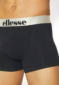 Schwarze Baumwoll-Boxershorts mit einem silbernen elastischen Bund, der das Logo "ellesse" in Schwarz zeigt. Glatte Textur mit einer figurbetonten Passform.
