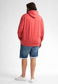 Felpa corallo con cappuccio regolabile, abbinata a pantaloni shorts di denim arrotolati. Sneakers bianche con logo nero. Design semplice e casual.