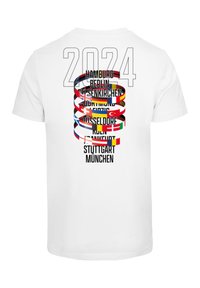 Hvit t-skjorte med en stor "2024" grafikk med bynavn og fargerike sirkulære flagg, ordnet vertikalt på baksiden.