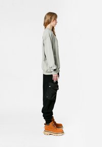 Sudadera oversized gris claro, joggers negros con un bolsillo lateral y botas de tan con cordones y suela gruesa blanca. Diseño simple, sin patrones.