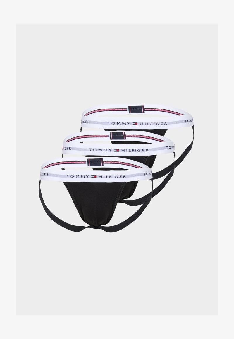 Trois paires de culottes thong noires avec des ceintures élastiques blanches ornées d'accents rouges et bleus, portant la marque "TOMMY HILFIGER."