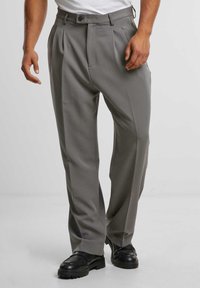 Pantalones grises con pliegues hechos de un tejido suave; presentan un cierre con botón, bolsillos laterales y un diseño de pierna recta. Complementan unos zapatos negros.