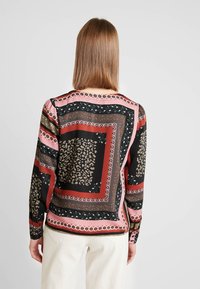 Camicetta a maniche lunghe nera, rossa e rosa con un motivo misto che presenta stampe animali e accenti floreali su un tessuto setoso.