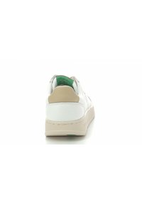 Zapatilla blanca con un exterior de cuero texturizado, capucha beige en el talón y forro interior verde. Presenta una puntera redonda y una suela plana de goma.