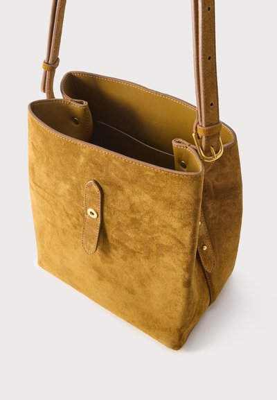 Καφέ σουέτ τσάντα ώμου με ρυθμιζόμενο ιμάντα, ανοιχτό πάνω μέρος και εσωτερική τσέπη ορατή σε λευκό φόντο.