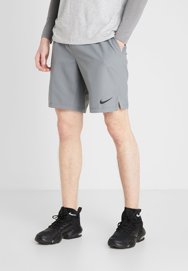Grå idrottsshorts med sidöppningar, med en svart Nike-logotyp. Bärs med svarta sneakers som framhäver en sportig look.
