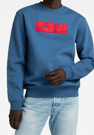 Blauwe sweatshirt van een katoenmix, met een rode logo aan de voorkant. De mouwen en de onderzoom zijn ribbelig, met een ronde halsontwerp.