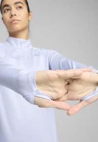 Un haut de sport à manches longues bleu clair avec un col à fermeture éclair demi-zip et des ouvertures pour les pouces, fabriqué en tissu extensible à texture lisse.