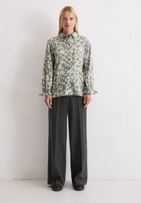 Light blue floral patterned shirt with button front, long sleeves, and ruffled cuffs; paired with dark gray wide-leg trousers.