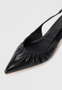 Mustapasta nahkainen slingback-mokkasiini, terävä kärki, rypistetty elastinen yksityiskohta aukossa, sileä pinta, litteä pohja, jossa minimaalista varustelua.