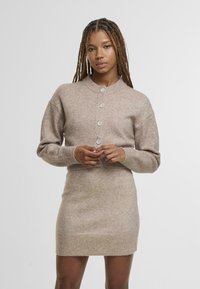 Gaiši brūna trikotāžas džemperkleita ar apaļu apkakli, pogu detaļām priekšpusē un ribotām aprocēm un apakšu. Mīksta tekstūra, pieguļošs siluets.