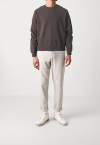 Felpa marrone scuro con polsini a costine, abbinata a pantaloni aderenti grigi chiari. Sneakers crema con dettagli texture completano l'outfit.