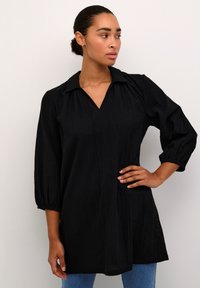 Chemise noire avec col, manches trois-quarts et décolleté en V. Tissu texturé avec une coupe confortable. Associée à un jean bleu.