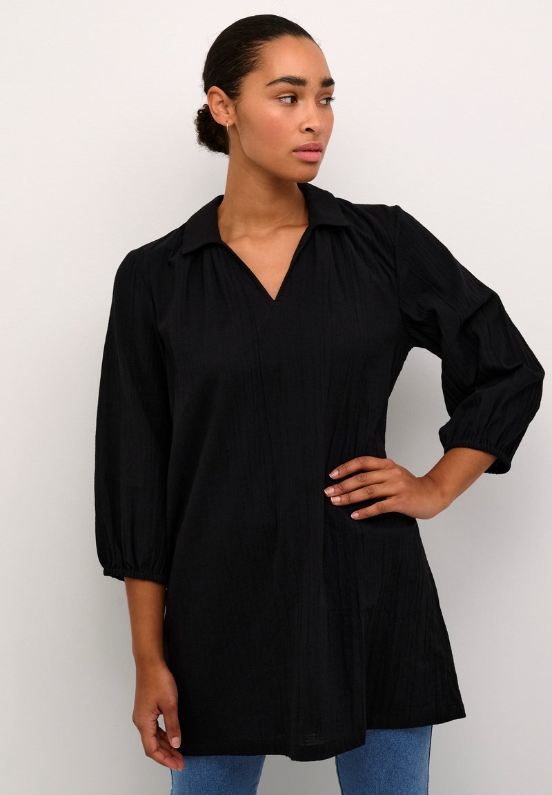 Chemise noire avec col, manches trois-quarts et décolleté en V. Tissu texturé avec une coupe confortable. Associée à un jean bleu.