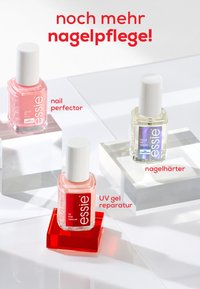 Drei Essie Nagelpflegeprodukte: ein rosafarbener Nagellack, ein klarer UV-Gel-Reparierer und eine härtende Formel mit holografischem Etikett, präsentiert auf klaren Sockeln.