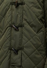 Veste matelassée vert foncé avec fermetures à boutons à bascule et une seule poche inclinée visible du côté droit.
