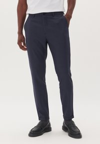 Navyfärgade dressade byxor med ett subtilt rutmönster, smal passform, sidofickor och uppvikta avslut. Kombineras med svarta läderskor.