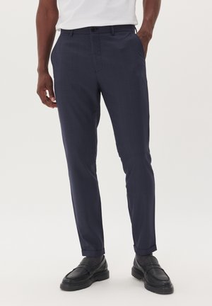 Pantalons de costume bleu marine avec un motif à carreaux subtil, coupe slim, poches latérales et ourlets retroussés. Associés à des chaussures en cuir noires.