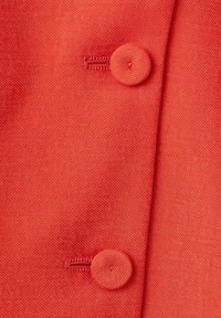 Tissu rouge avec deux boutons ronds recouverts de tissu et des boutonnières, montrant une texture et des coutures détaillées.