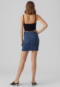 Denim mini krilo s ravnim rezom, zbledela modra barva in dvema zadnjima žepoma, v kombinaciji z črno kratko majico in črnimi sandalčki s odprtimi prsti.