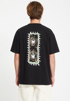 Schwarzes Baumwoll-T-Shirt mit einem großen grafischen Design auf der Rückseite, das Augen zeigt, die von gezackten Kanten in grünen und beigen Farbtönen umrahmt sind.