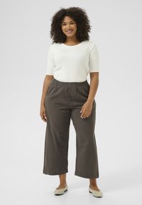 White three-quarter sleeve top paired with loose, dark brown cropped pants. Smooth fabric and elastic waistband for comfort. Light shoes complete the look.