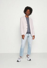 Light pink blazer with lapels, beige knit top, light blue straight-leg jeans, and white sneakers with black accents. Smooth texture throughout.