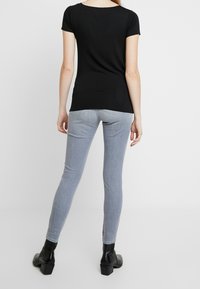 Černý top s krátkým rukávem v kombinaci s úzkými světle šedými džínami. Outfit je doplněn černými kotníkovými botami s robustním podpatkem.