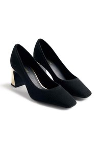 Zapatos de tacón alto de punto negro con puntera afilada y un tacón cuadrado en forma de bloque en metálico dorado y negro. Textura suave y diseño elegante.