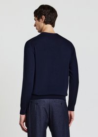 Marineblauer Pullover mit langen Ärmeln, rundem Halsausschnitt sowie gerippten Bündchen und Saum. Getragen mit karierter Hose. Glatte Textur.